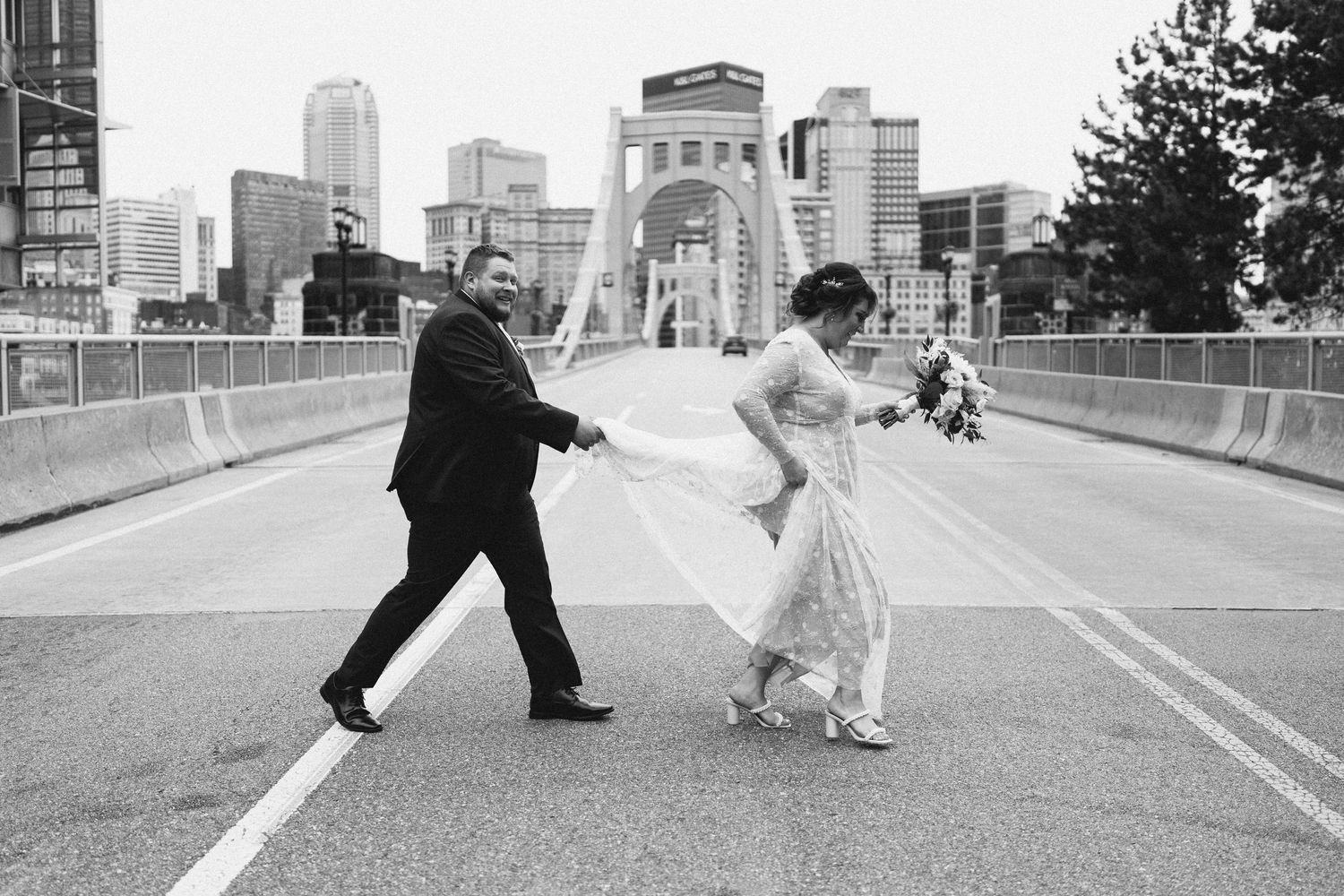 A couple dances playfully on a bridge with a cityscape in the background.