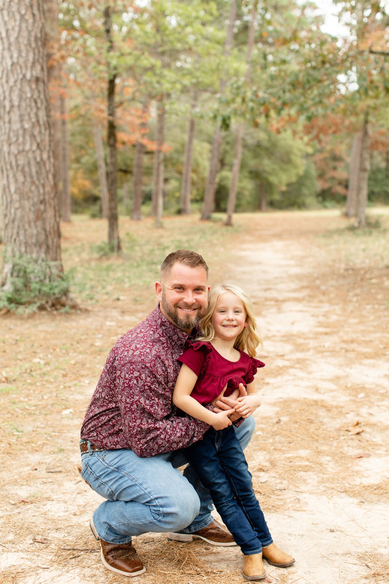 A father and child share a playful moment on a forest path during autumn.