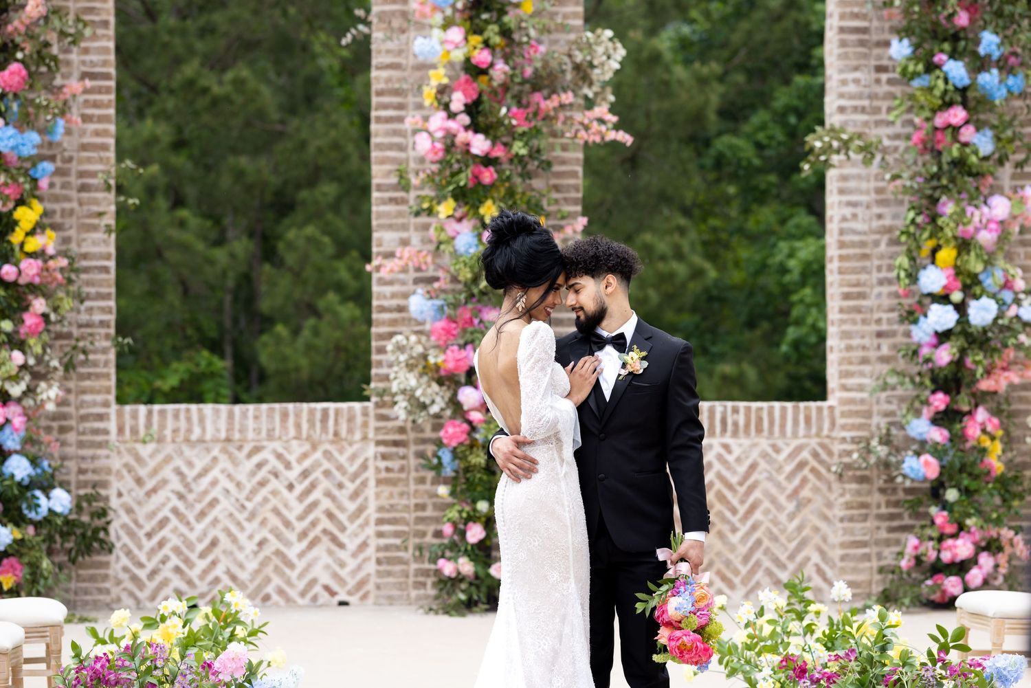 A romantic wedding ceremony under a floral-decorated brick archway.