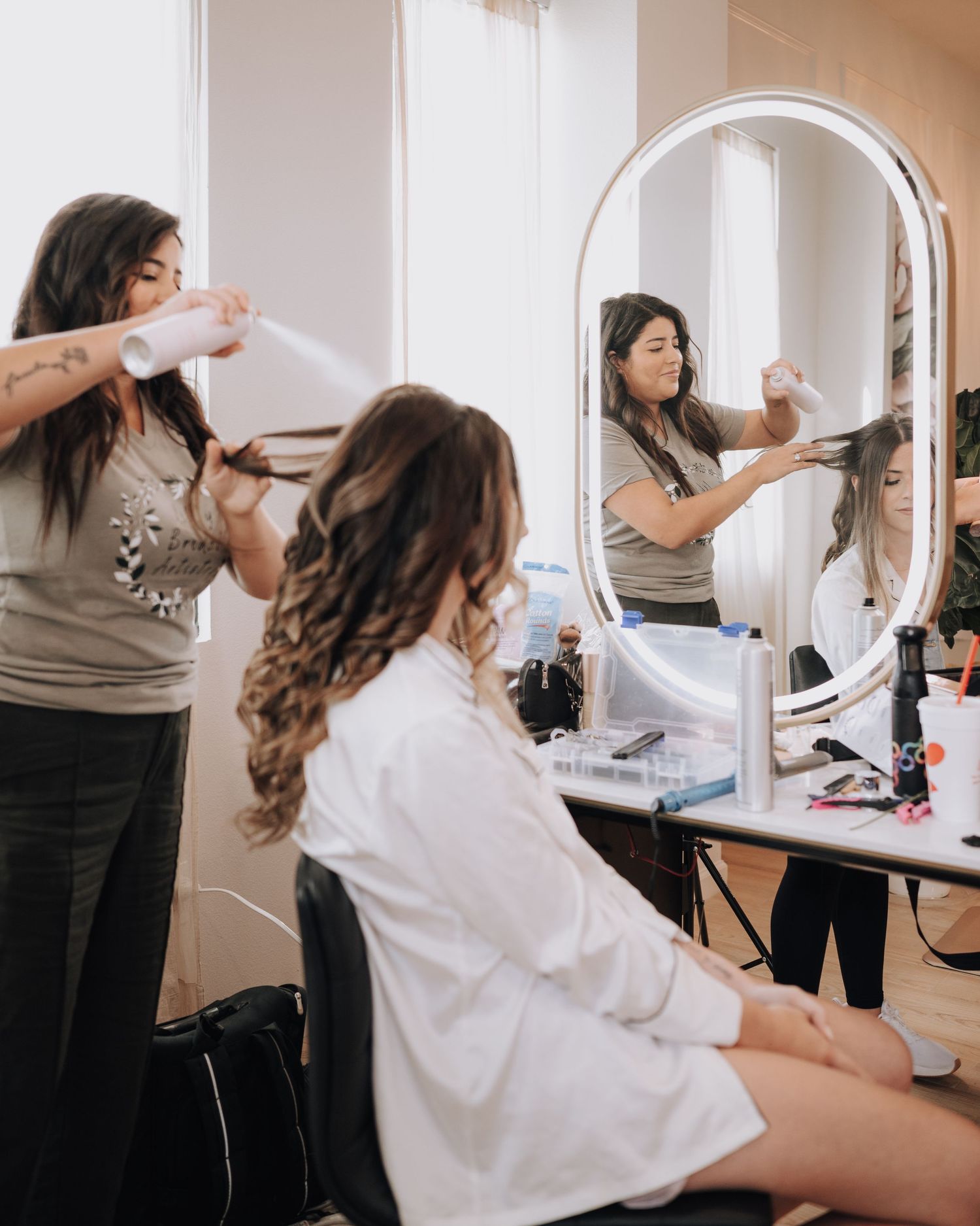 Hair stylist working on client's hair in front of a professional vanity mirror setup.