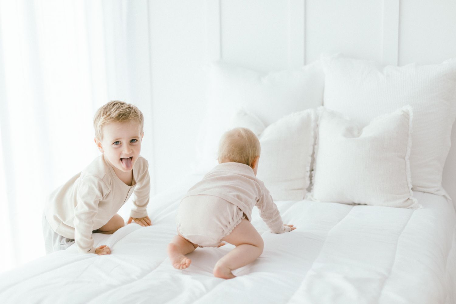 Baby crawling on white bedding in bright, airy room.
