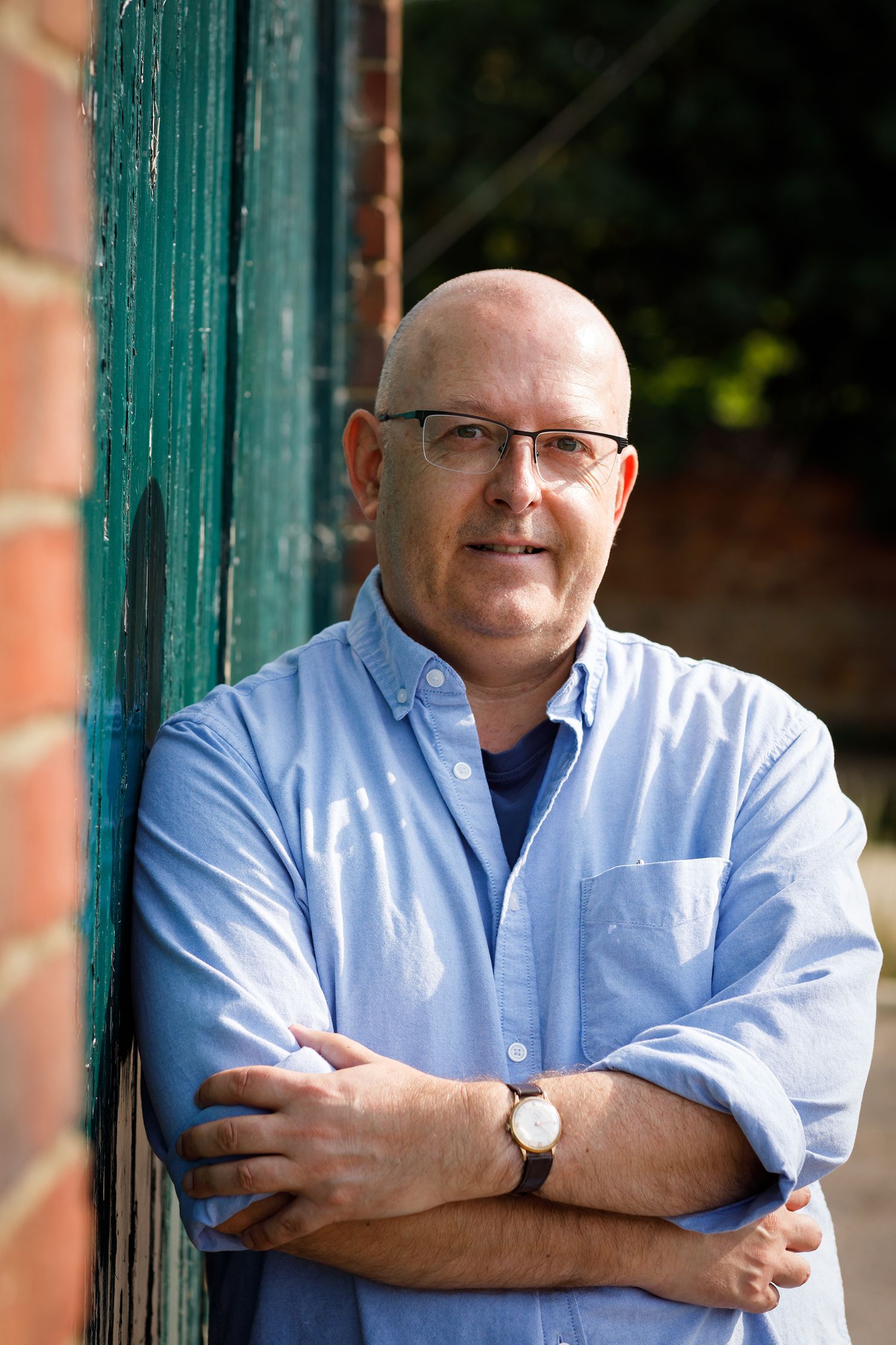 Person wearing blue button-down shirt and glasses poses next to green painted column during business branding photoshoot