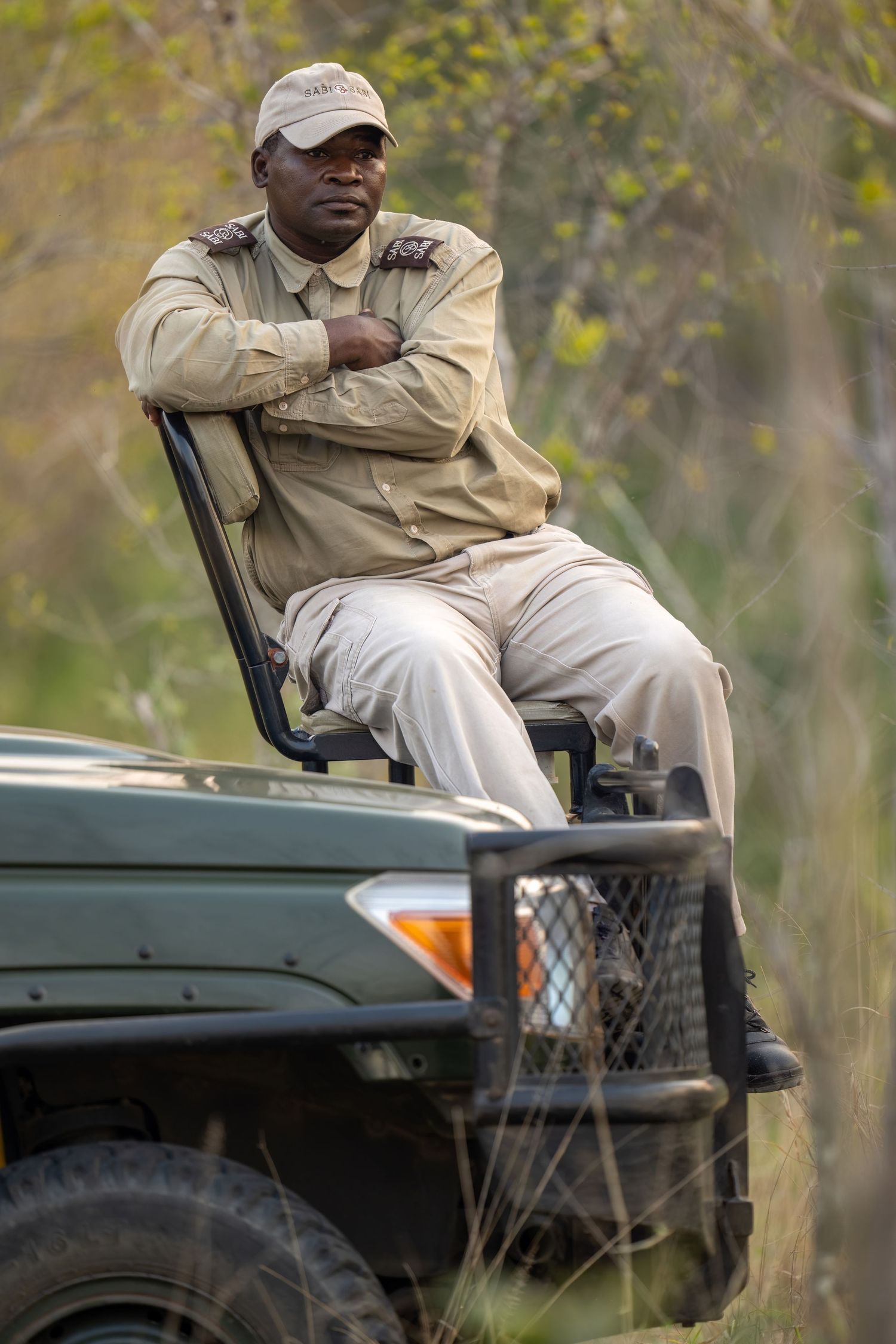 Safari guide seated on a game viewing vehicle in khaki uniform.