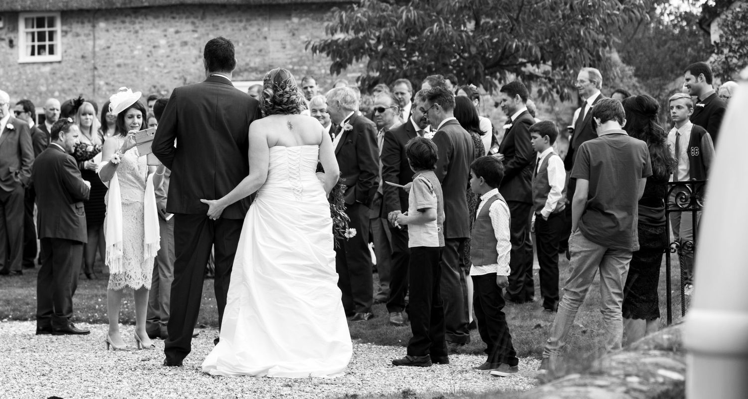 Black and white panoramic sequence showing wedding guests gathering outdoors for group photos.