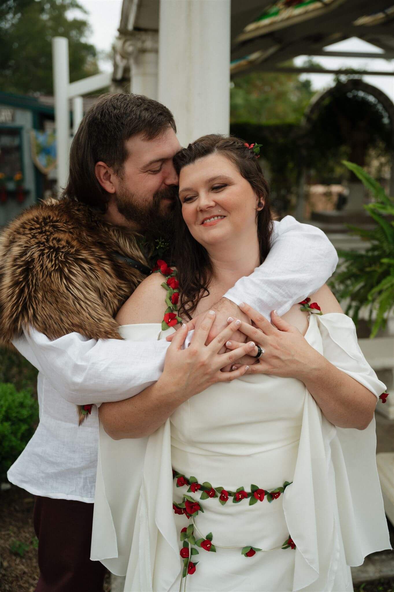A romantic renaissance-themed wedding couple embraces under a white pergola with fur and floral details.