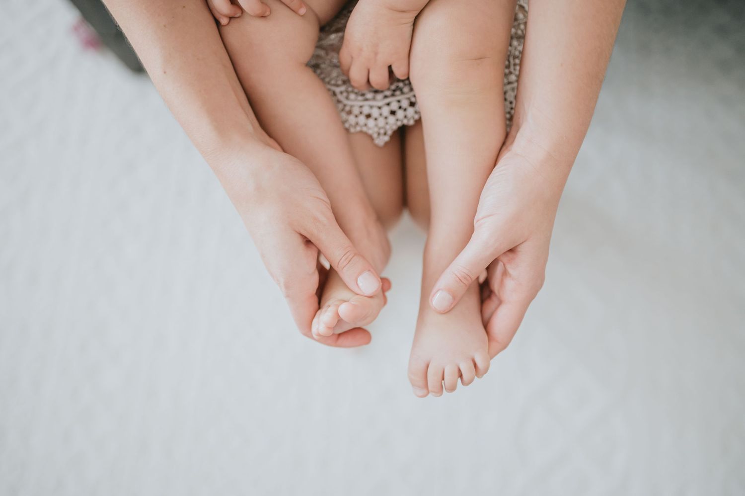 Close-up view of hands gently touching bare feet on a white surface.