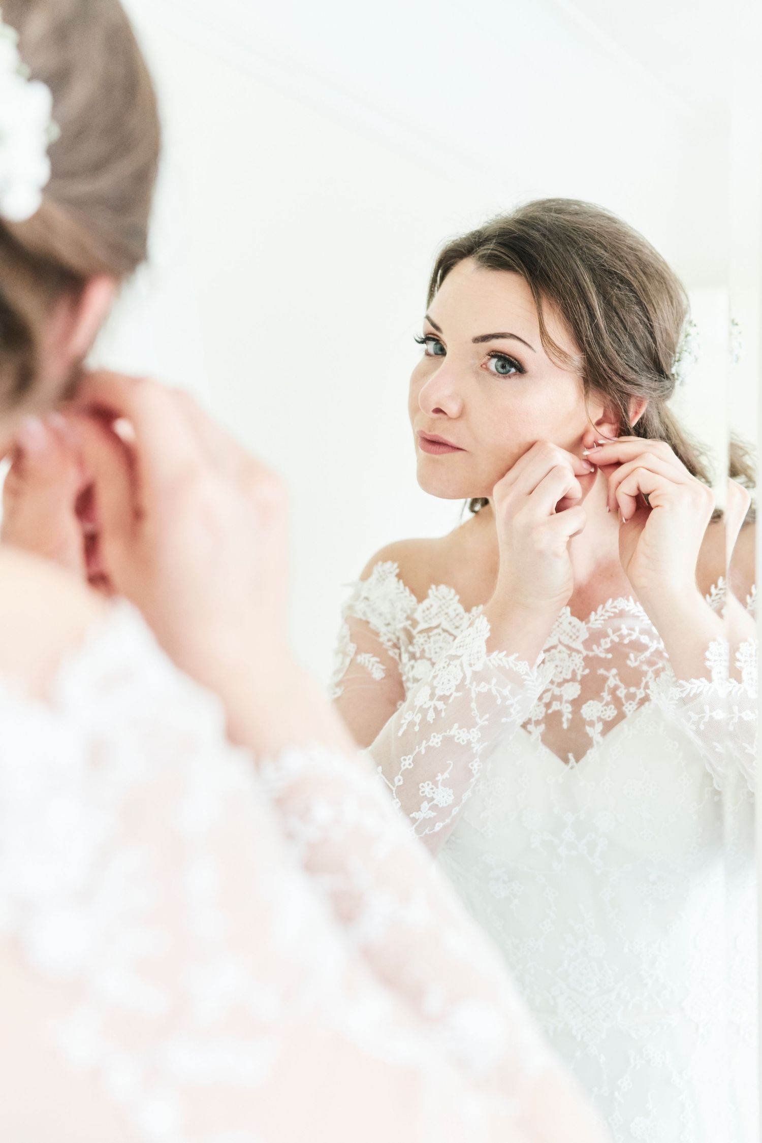 bride putting in earrings in front of mirror at Orsett Hall, Essex. by Norwich wedding photographer Faye Amare