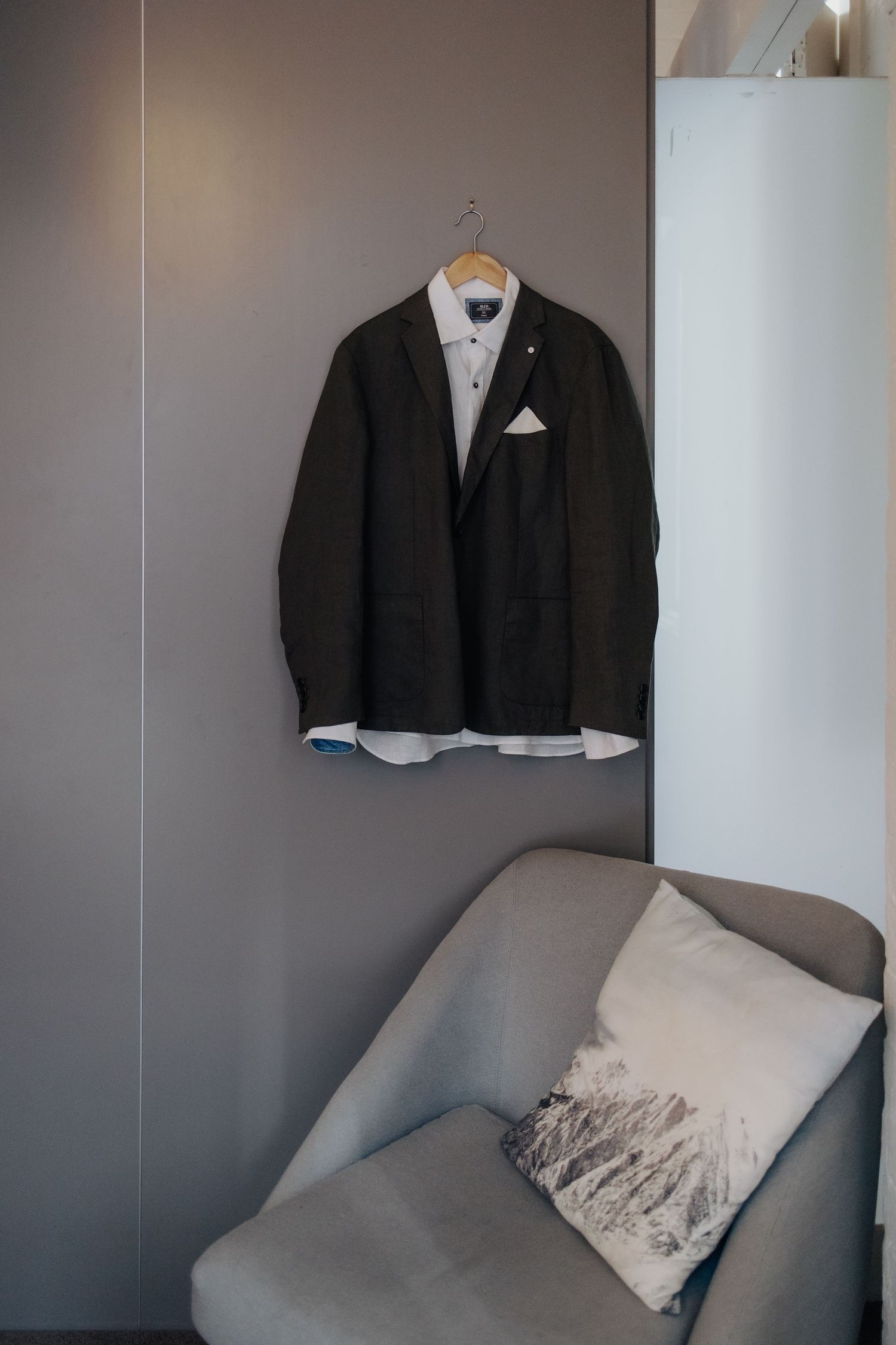 Black formal suits and jackets hanging on hangers against a grey wall in a room.