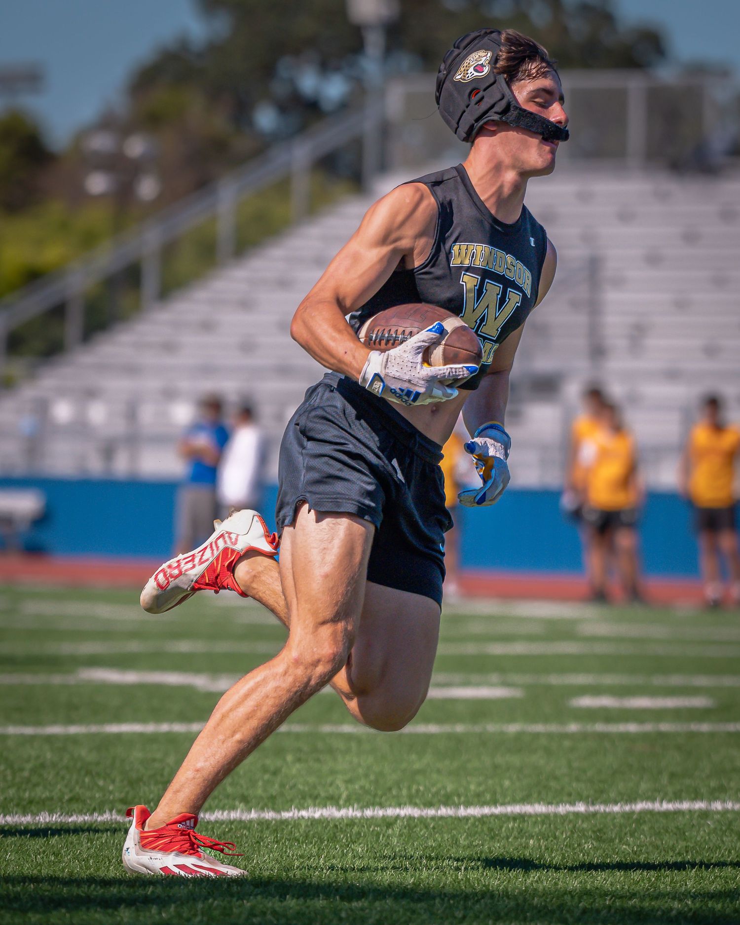 Rugby player in dark uniform sprints across field wearing protective face mask.