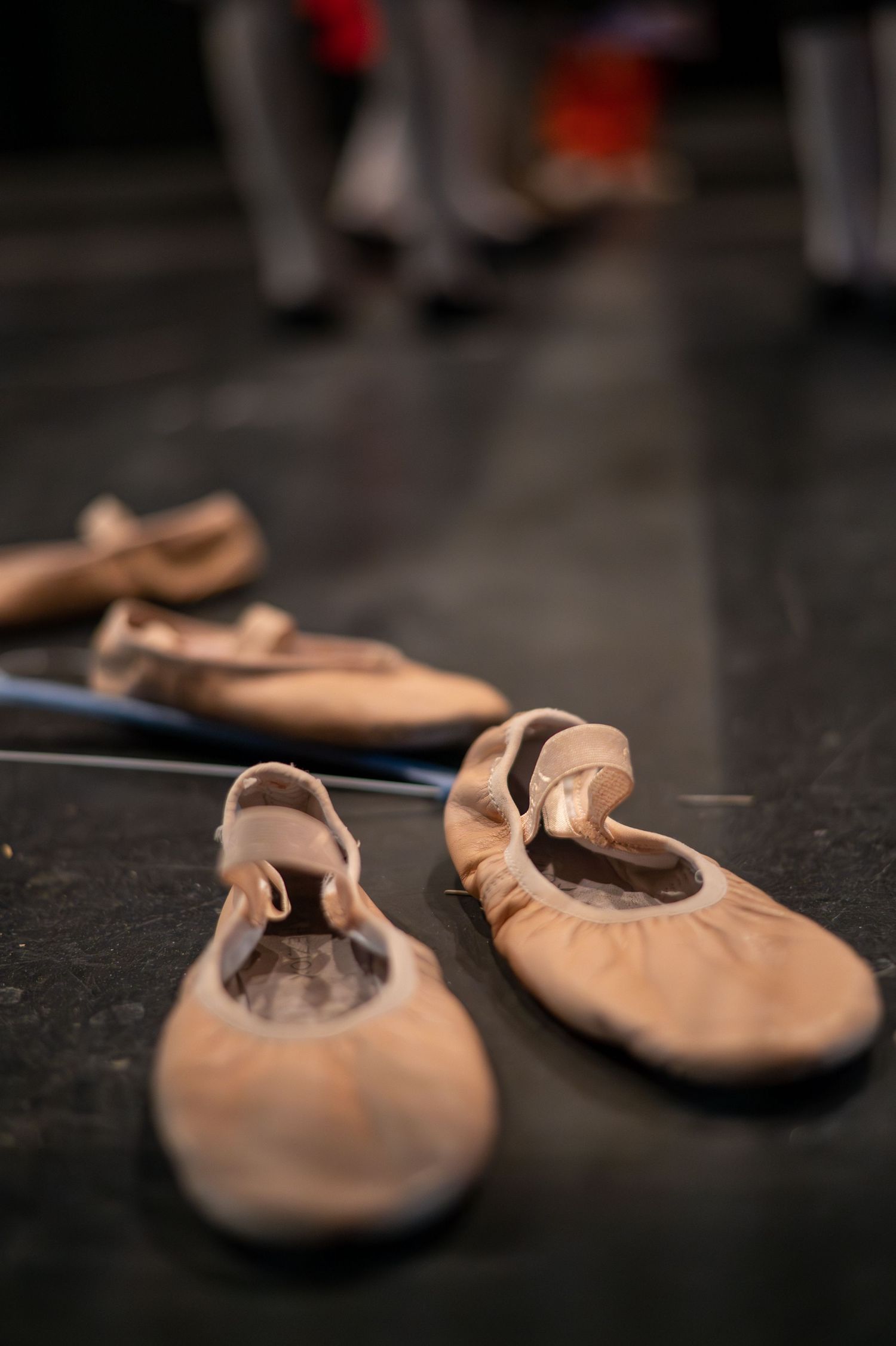 Pink ballet slippers arranged on dark floor with shallow depth of field.