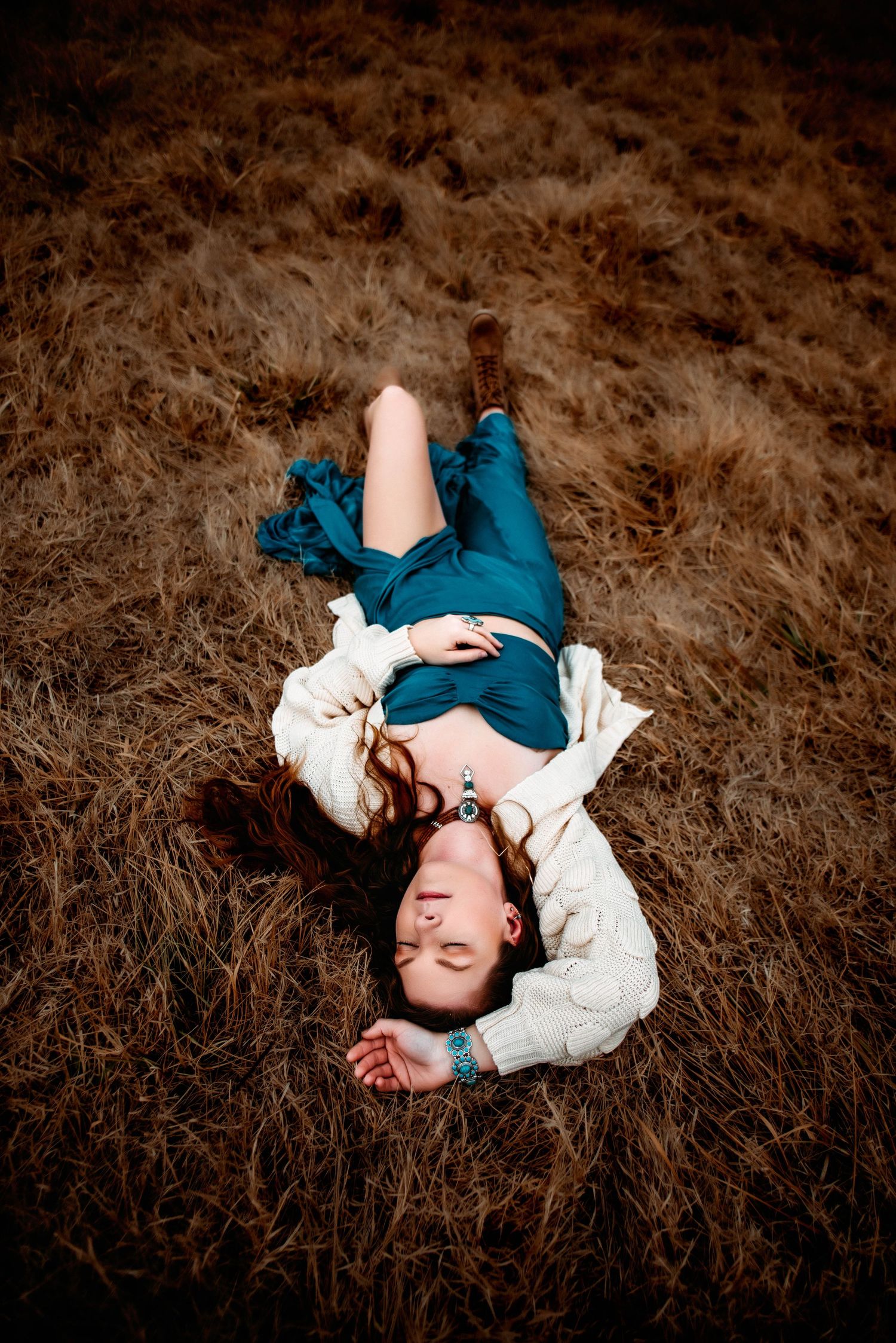 Artistic portrait lying in dried grass field wearing teal and white clothing.