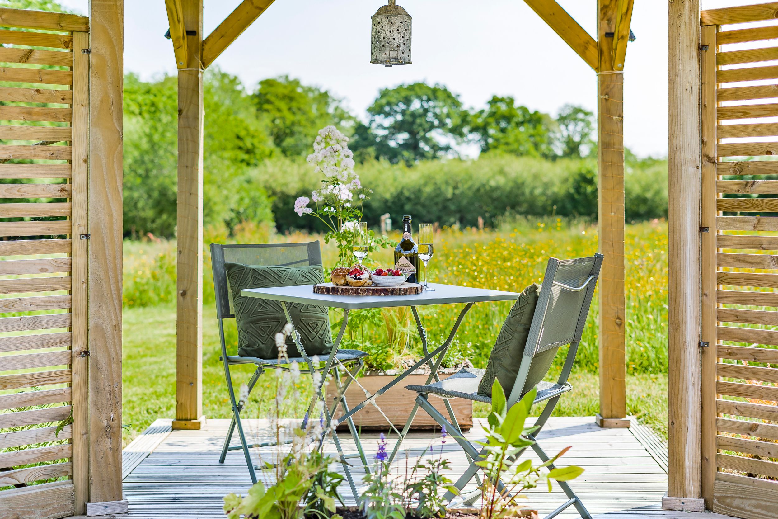 A modern outdoor seating area with wooden pergola and comfortable chairs surrounded by lush greenery.