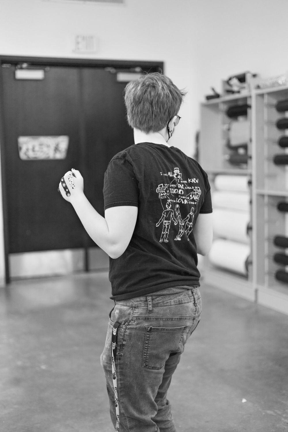 Black and white photo of someone wearing a graphic t-shirt shown from behind.