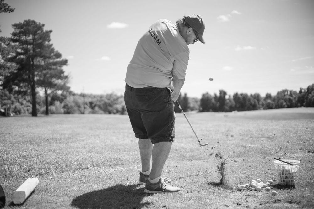 Black and white photo of a golfer preparing to putt on a sunny course.