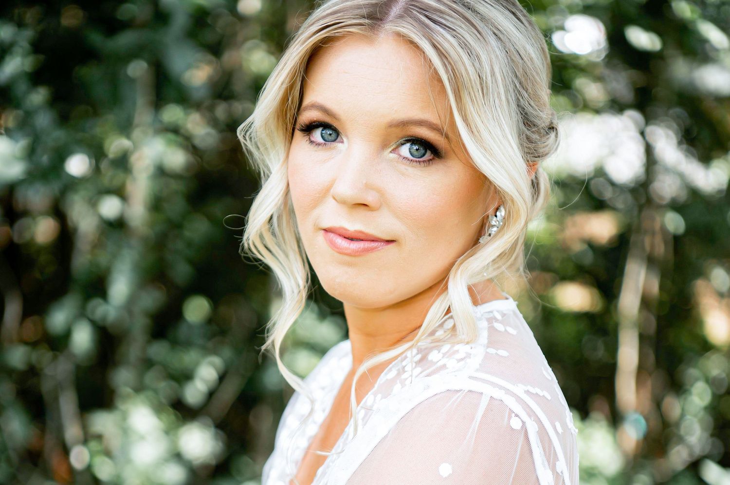 Bride in lace dress poses for portrait outdoors with soft natural lighting.