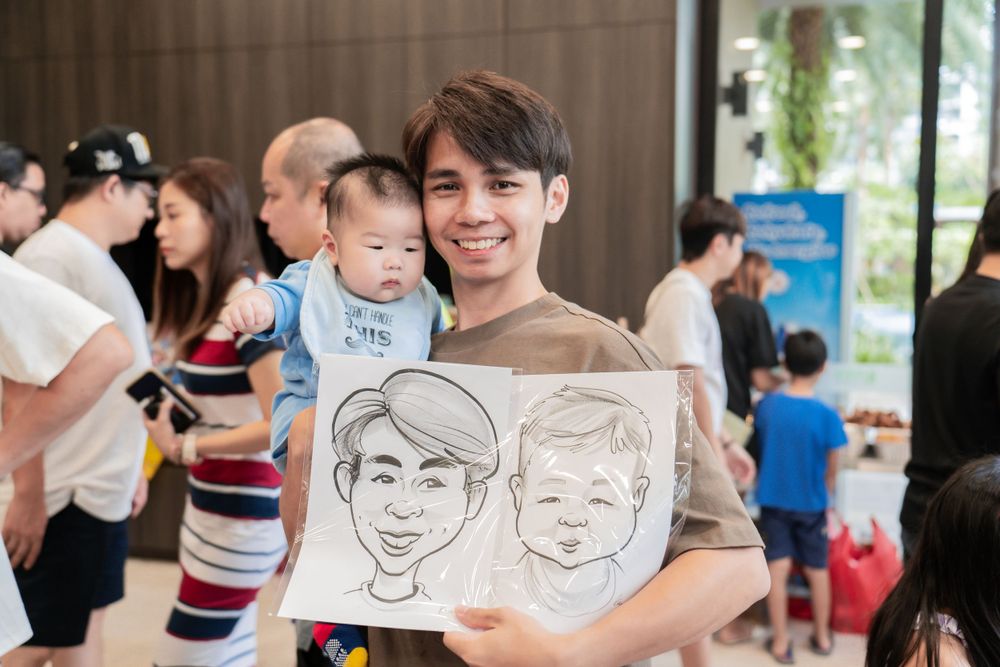 Someone holding portrait sketches of themselves and a child at an indoor event.