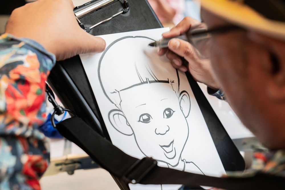Artist drawing a cartoon portrait sketch on black surface.