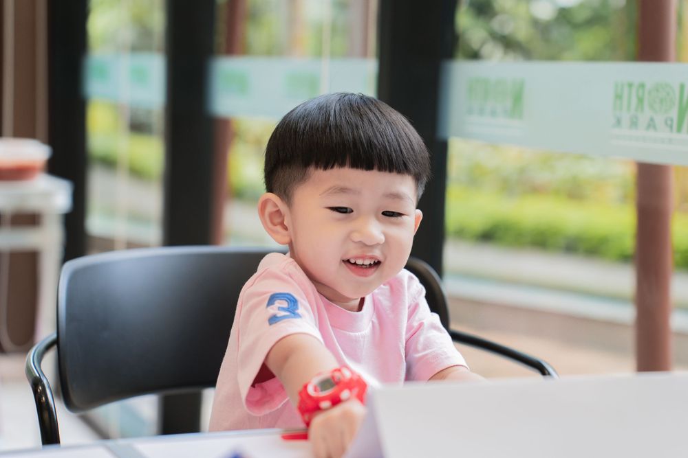 Young child in pink shirt smiles while seated at table during activity.