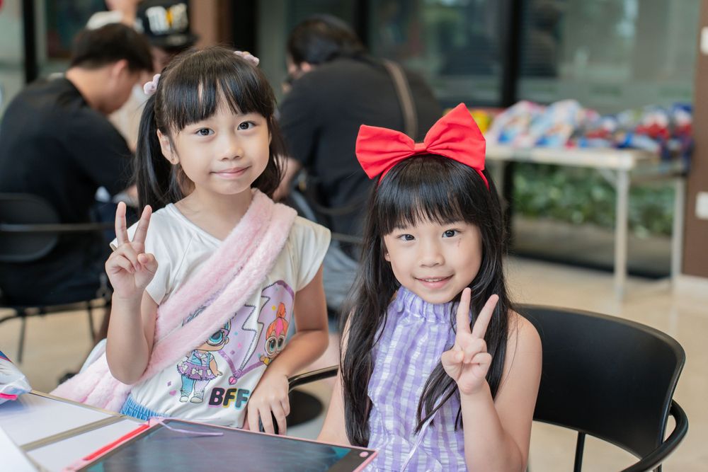 Two young children in pretty dresses making peace signs at a gathering.