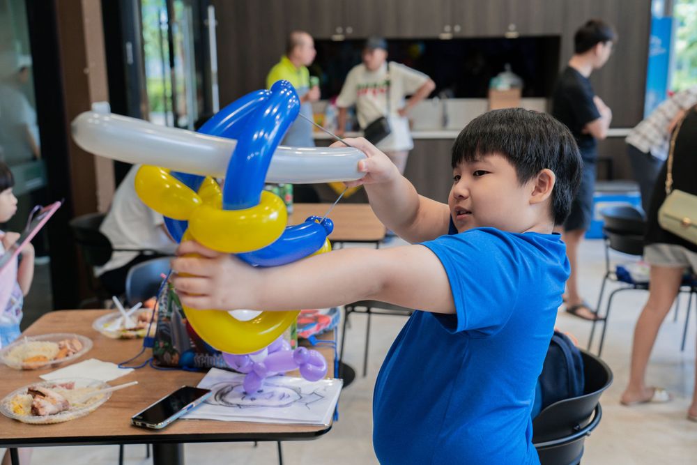 A child in blue plays with a balloon toy at an indoor gathering.