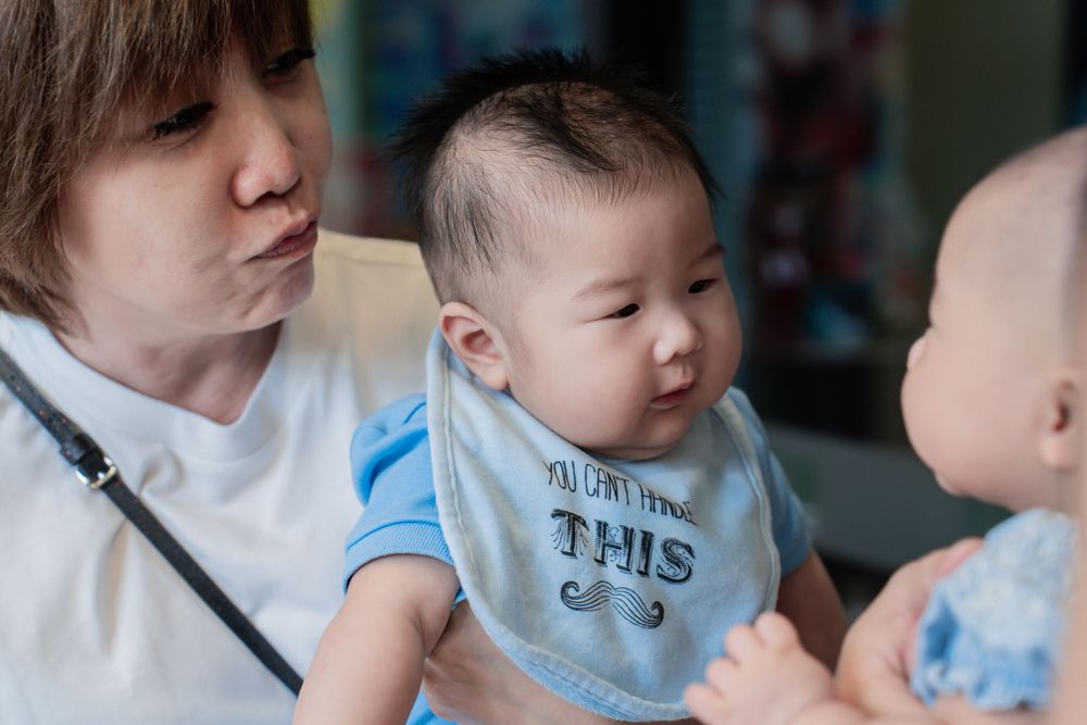 A baby wearing a blue bib being held at what appears to be a social gathering.