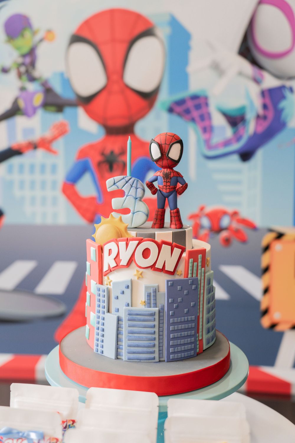 A Spider-Man themed birthday cake featuring a cityscape design and character topper.