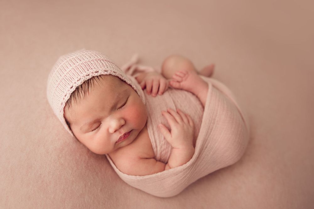 Newborn baby wearing pink knit hat wrapped in soft pink fabric.