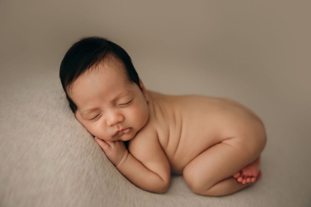 Peaceful sleeping newborn baby in artistic nude pose on beige backdrop.