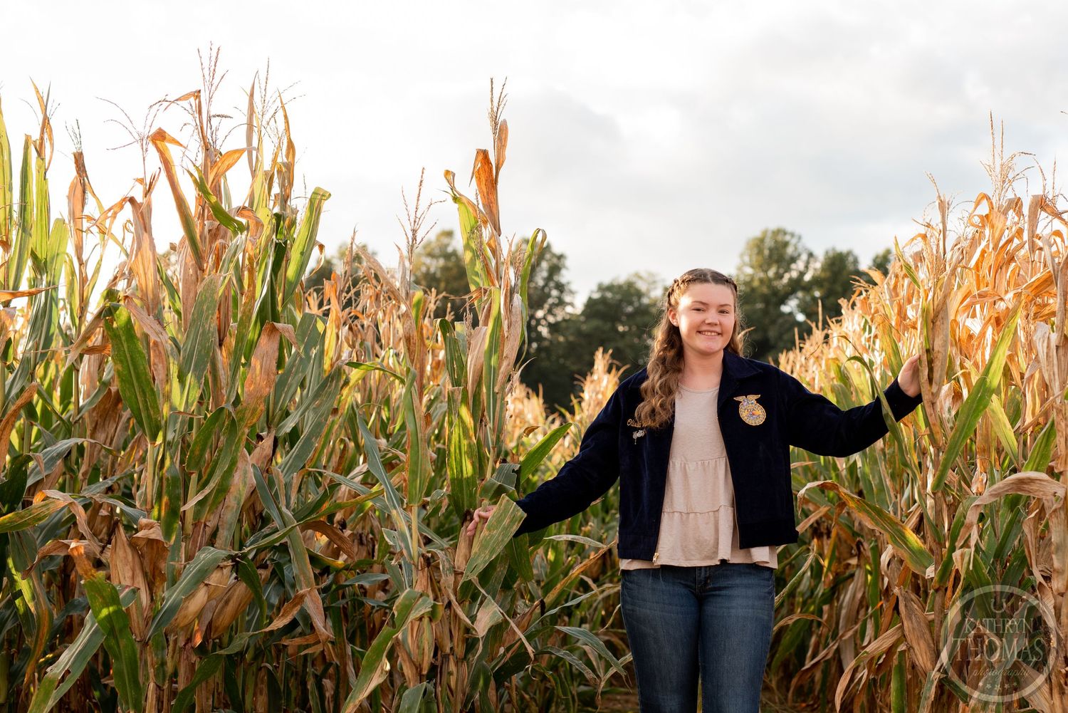 Standing joyfully in a cornfield while wearing a dark jacket at sunset.
