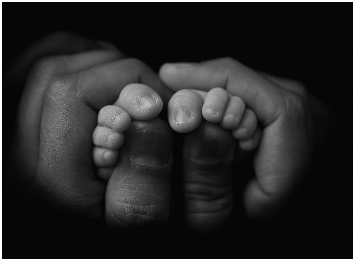 Close-up of dad holding newborn’s toes, baby’s toes curling around his thumbs