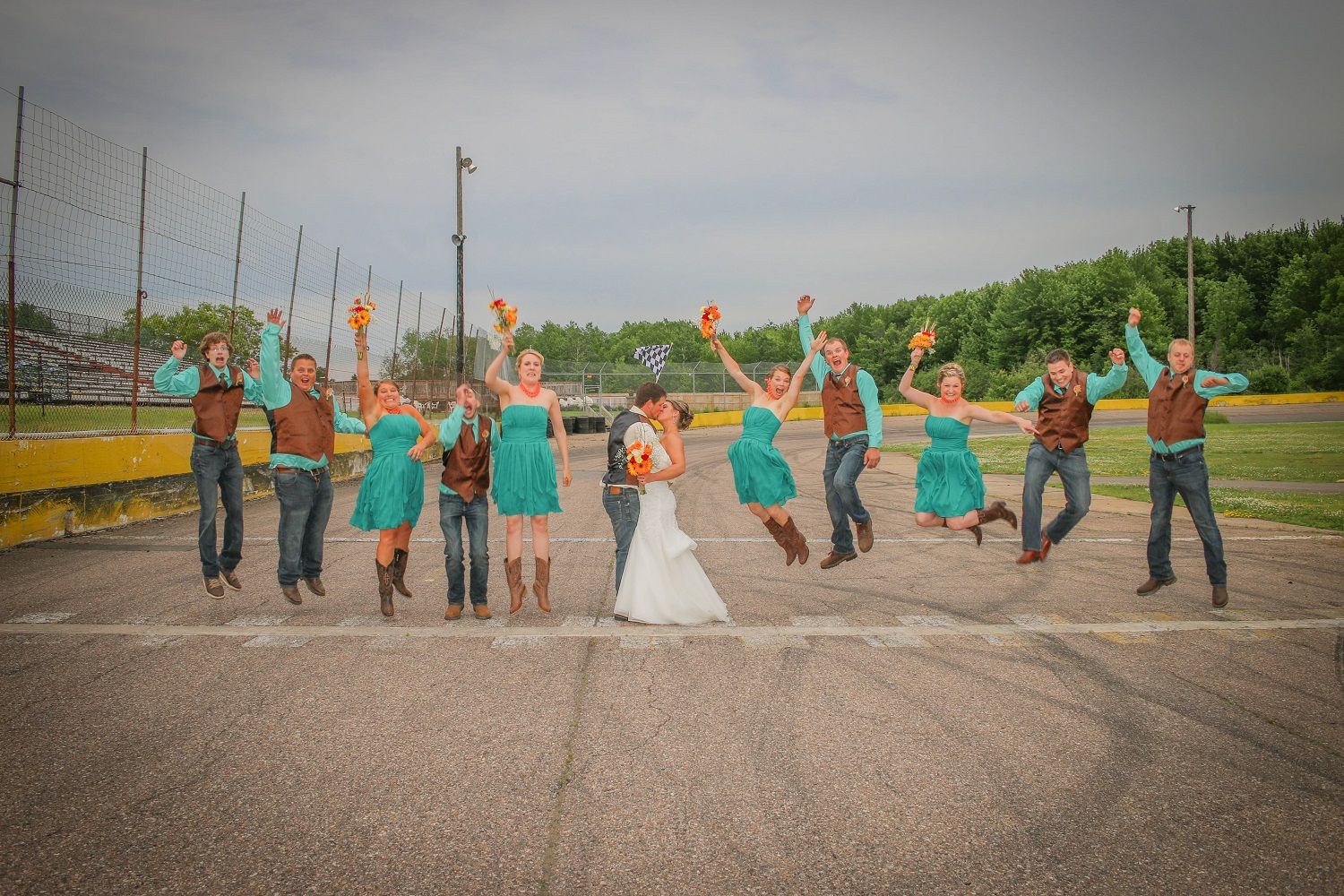 Wedding party poses joyfully in a line outdoors with matching teal dresses and suits.