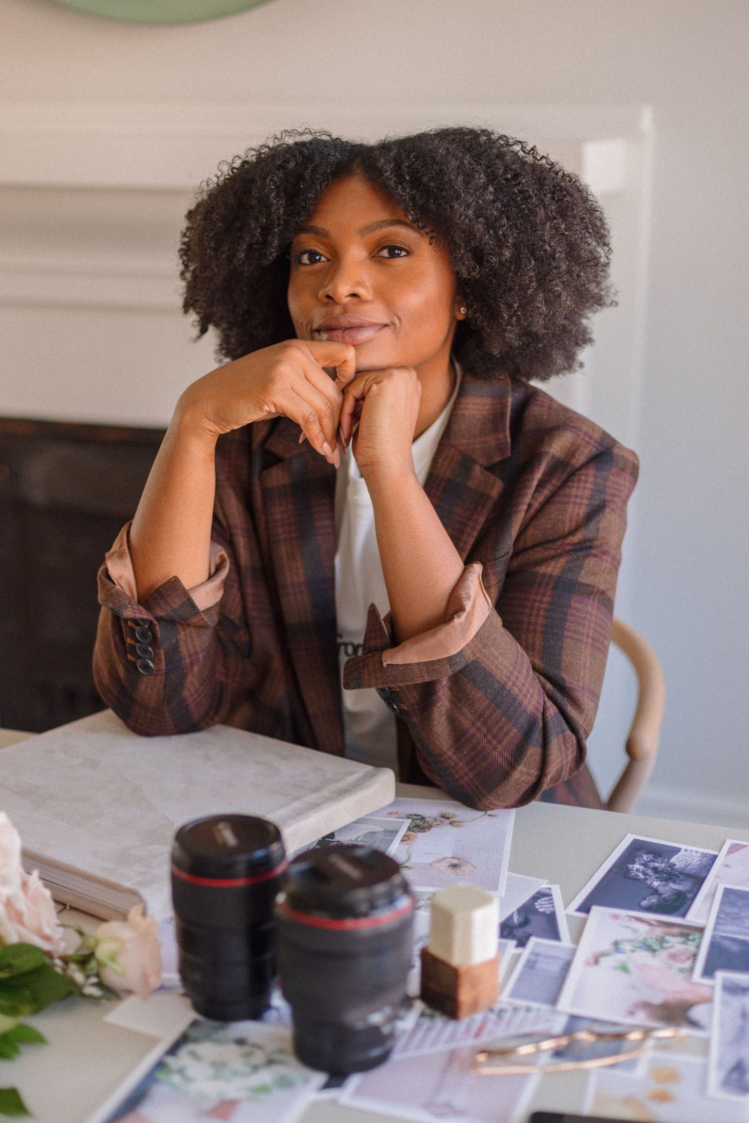 Workspace scene with camera lenses and photo prints featuring casual plaid outfit and natural curls.