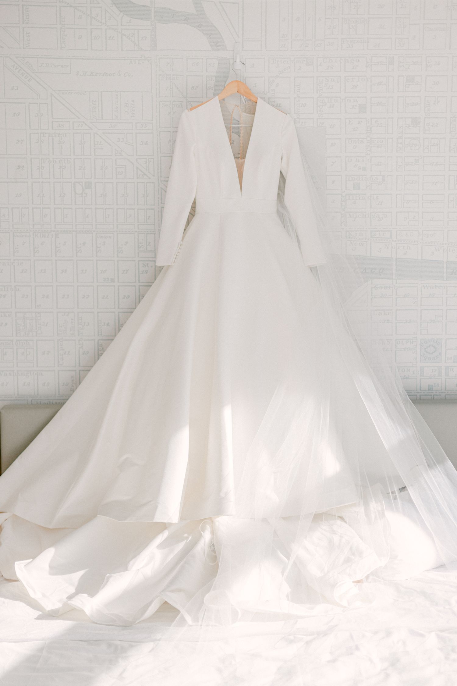 Elegant white wedding dress with long sleeves and full skirt hanging against a neutral background.