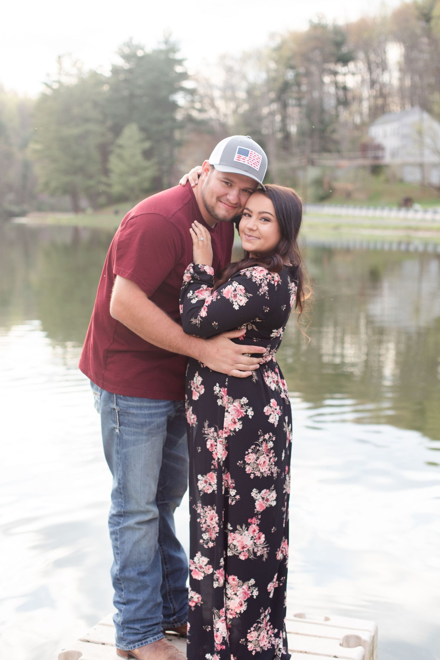 Romantic couple poses on dock by lake, wearing coordinated burgundy and floral black dress outfits.