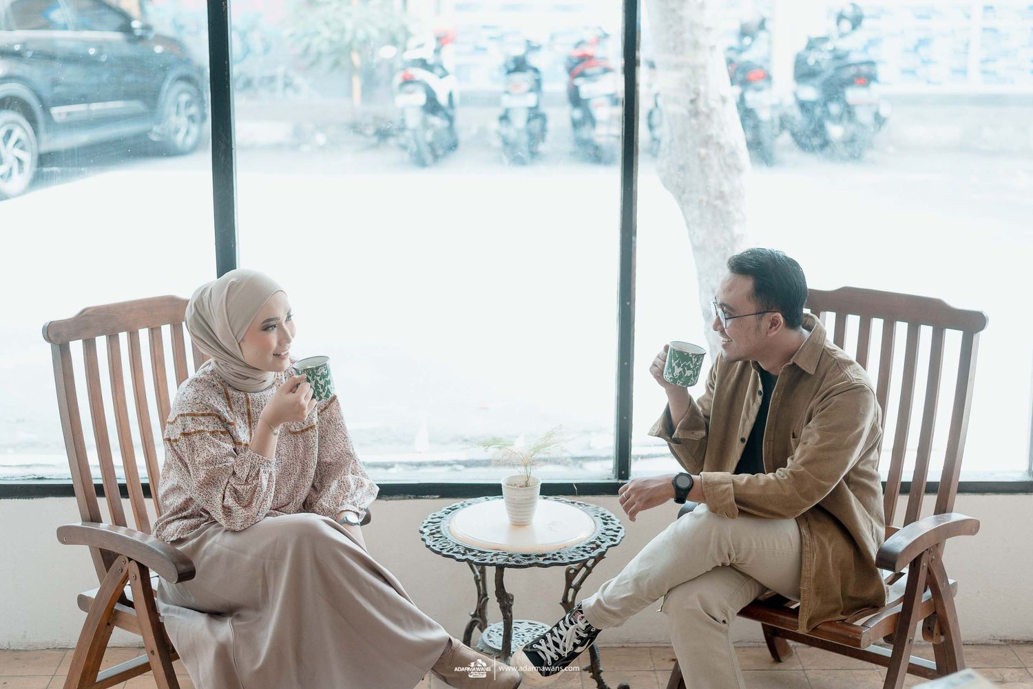 Two people enjoying a coffee date while sitting in wooden chairs by a window in a cafe.