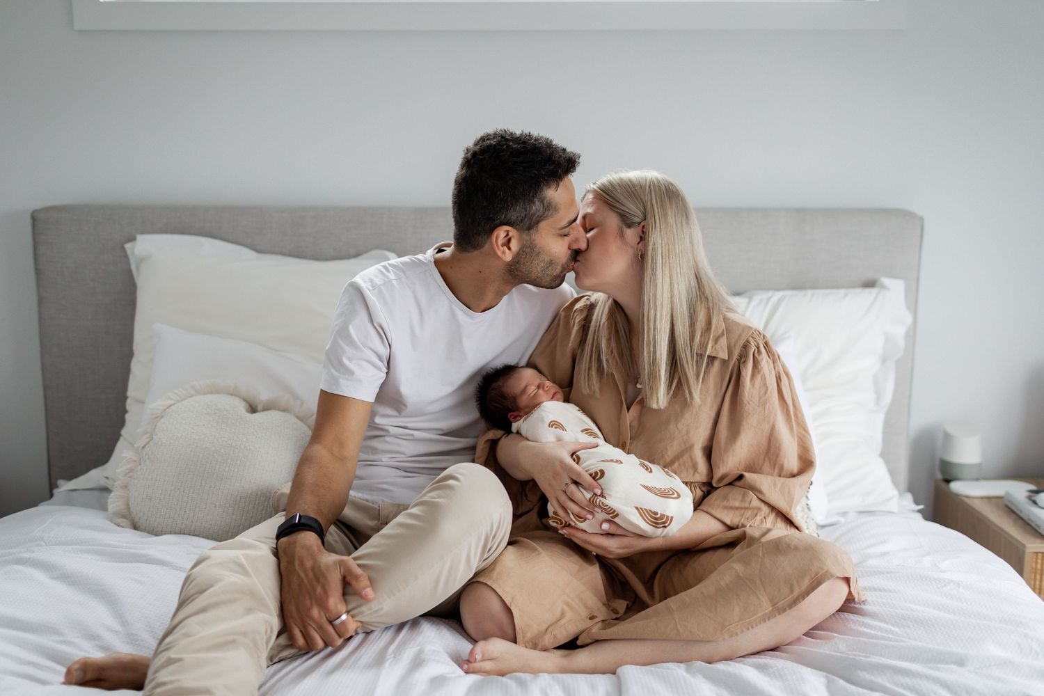 Intimate moment shared on a bed with white bedding and soft natural lighting.