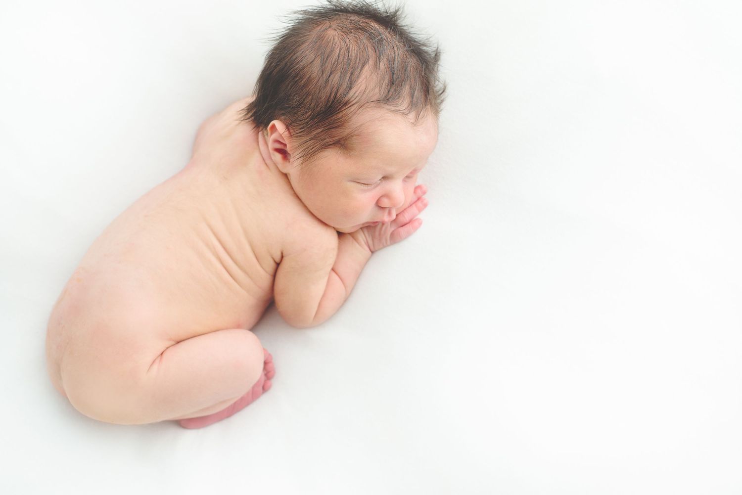 naked newborn baby boy laying on his stomach posing for a newborn photo in all white natural light studio in houston