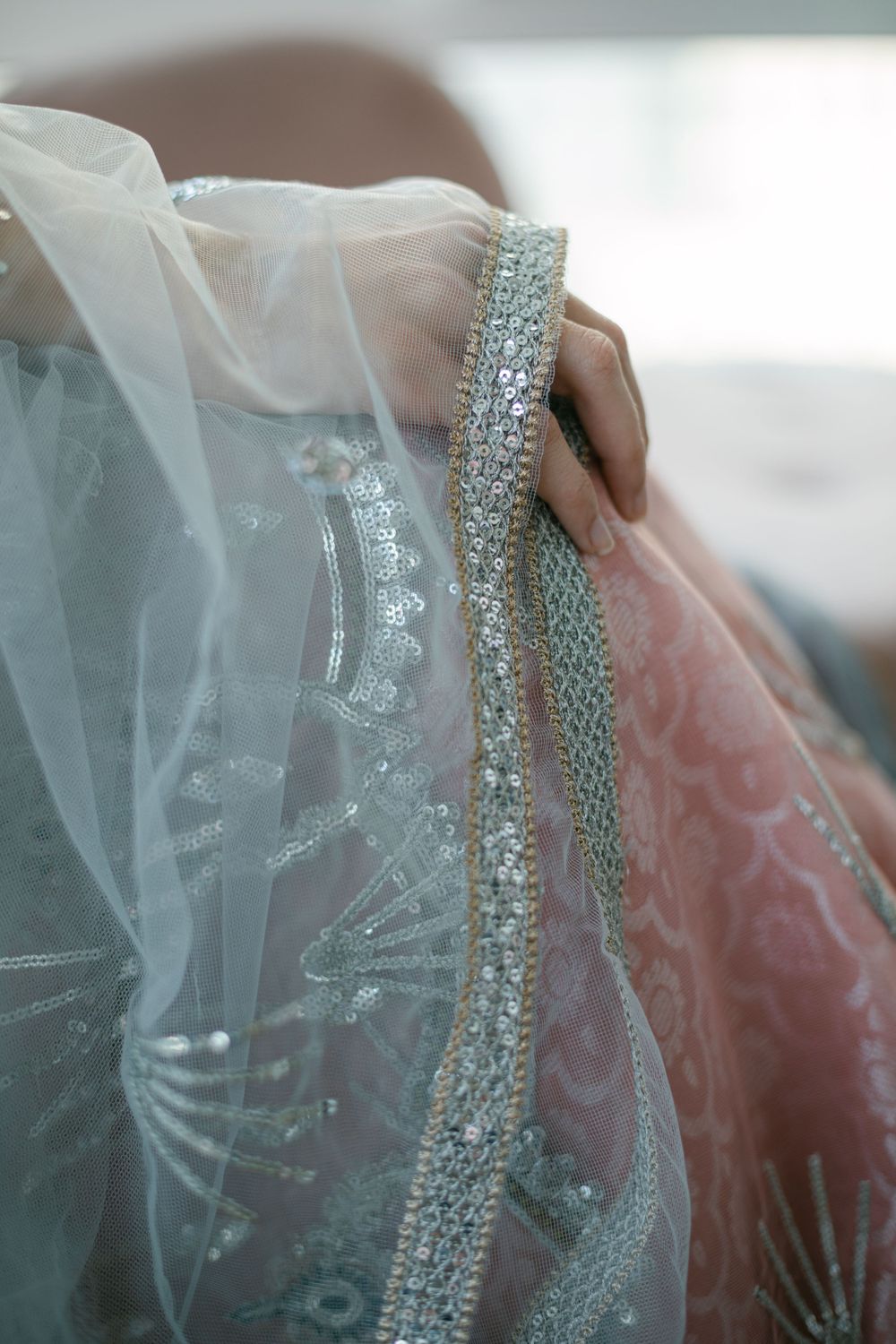 Intricate beaded details and delicate sheer fabric from a formal dress against a soft background.