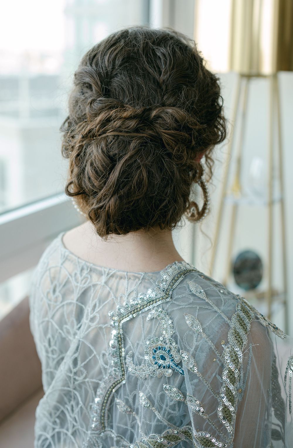 Elegant updo hairstyle with braided details shown from behind against a window.