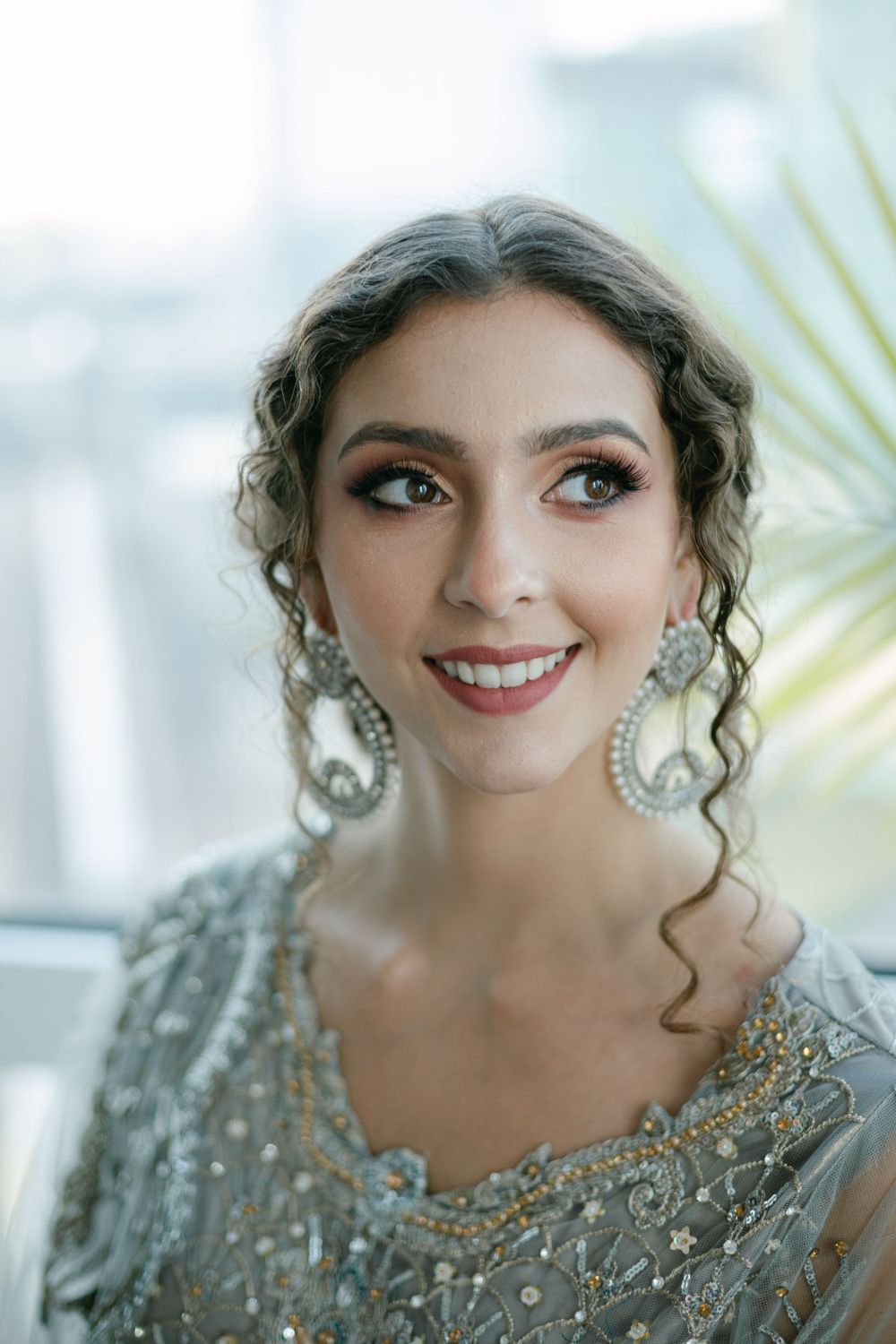 A close-up portrait showcasing ornate pearl earrings and a silver beaded wedding dress.