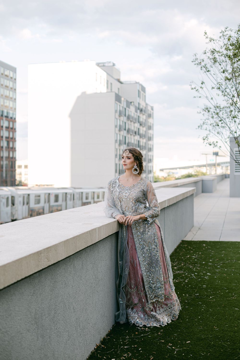 Elegant silver gown photographed on a rooftop terrace with city buildings in background.