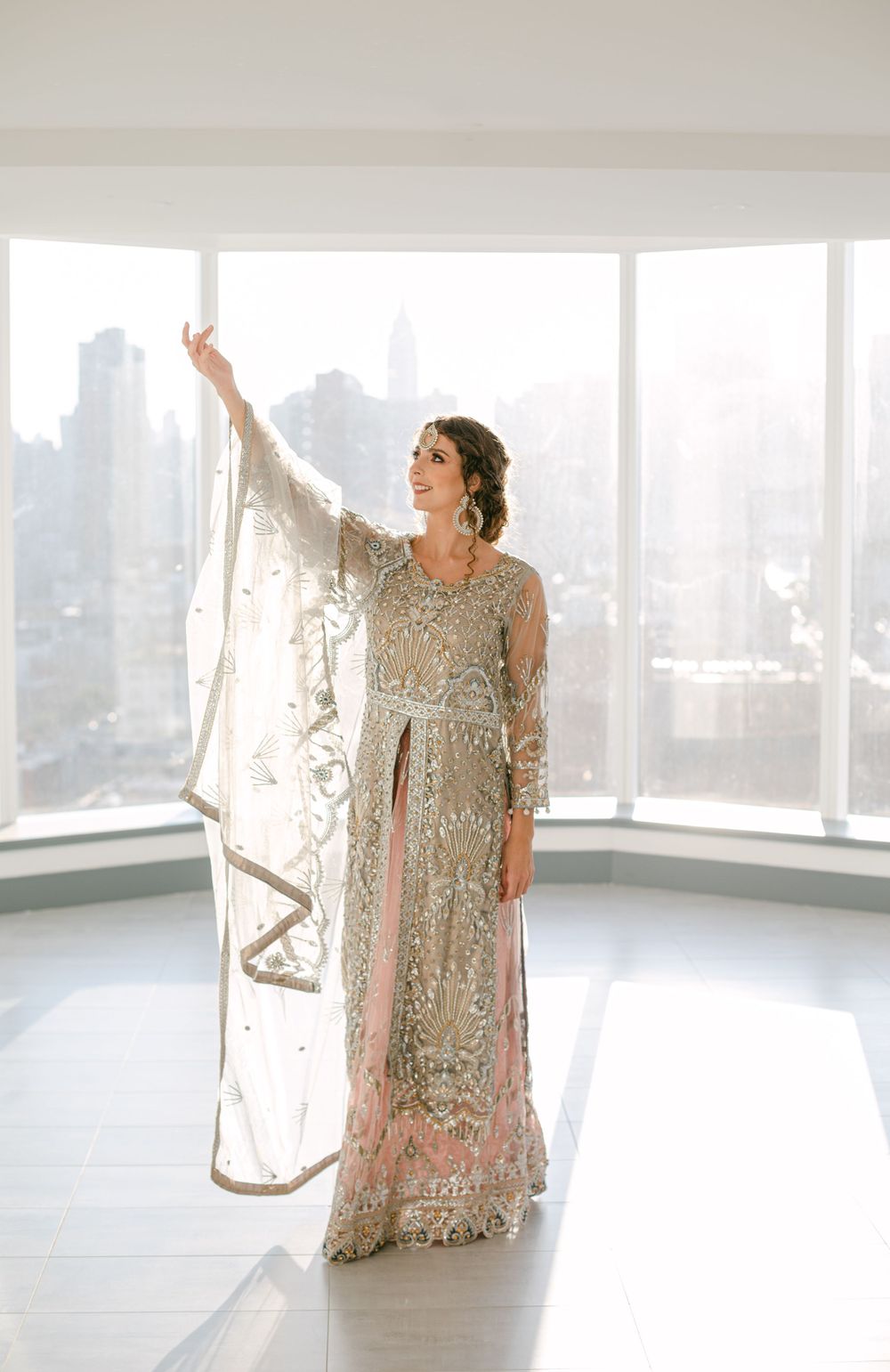 Ornate silver beaded gown with flowing cape photographed in bright modern room with city skyline view.