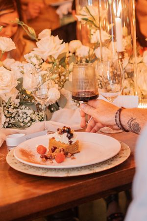 A plated dessert with berries and white flowers on an elegantly set dinner table.