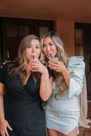 Two friends having fun while drinking cocktails at an indoor event.