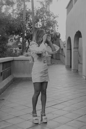 Woman in white dress posing on a terrace with Spanish colonial architecture.