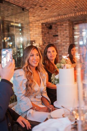 An elegant celebration dinner with a white cake and floral decorations in a brick-walled restaurant space.