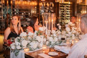 A candlelit dinner table decorated with white floral arrangements and tall glass candle holders in an elegant restaurant setting.