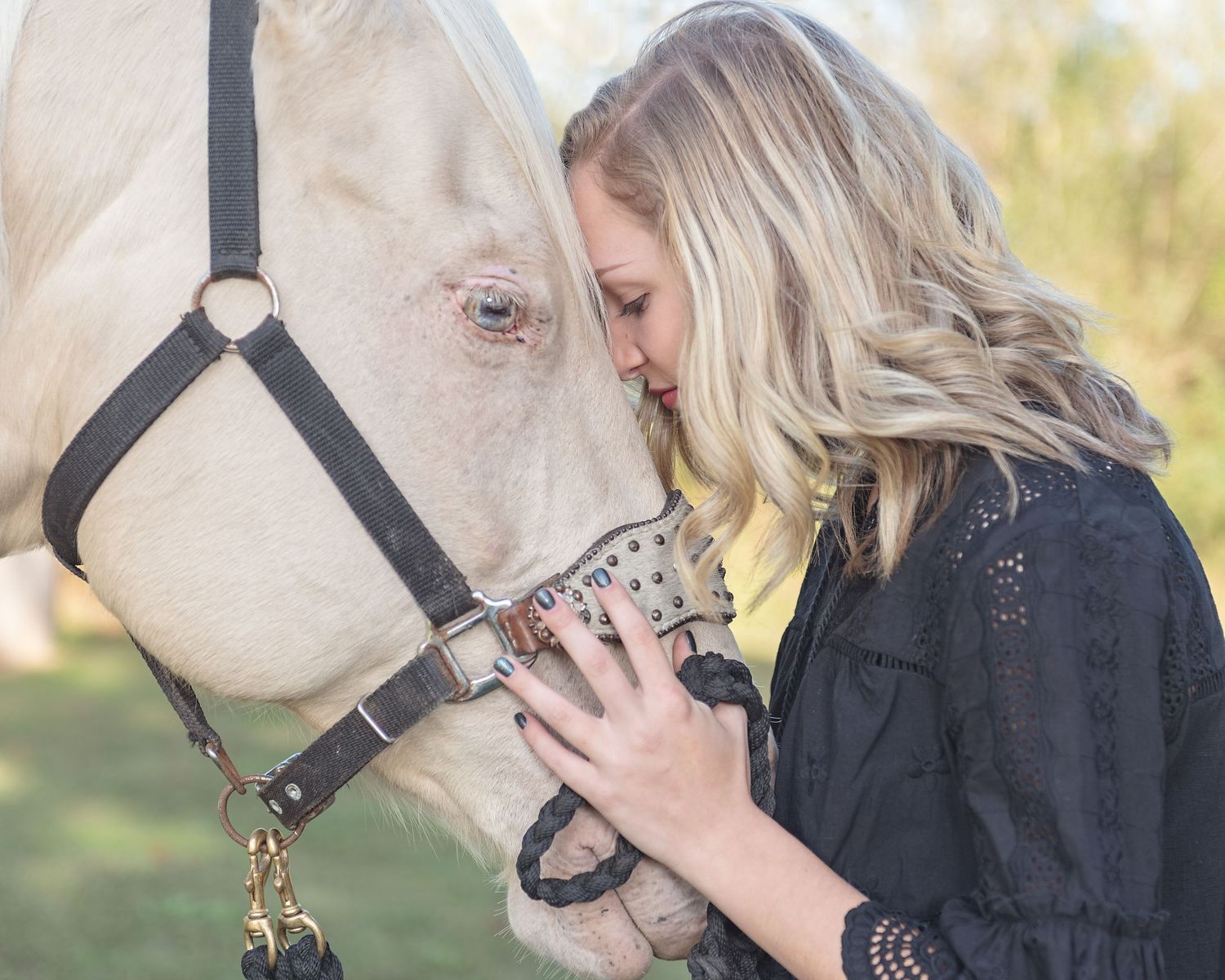 Blonde girl, head to head with blue eyed cremello horse