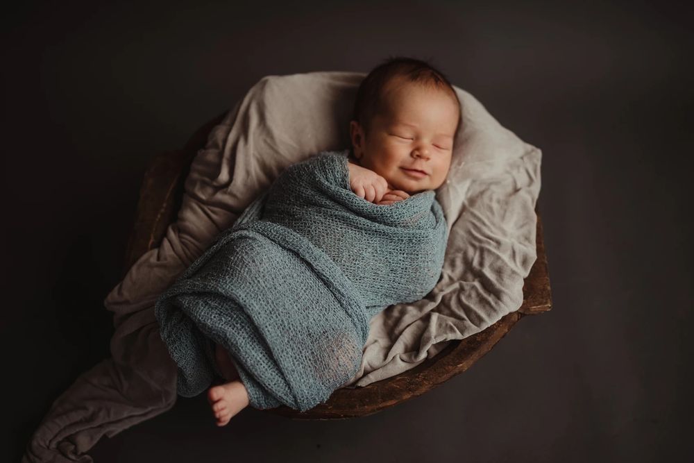 Sleeping newborn wrapped in soft gray swaddle on neutral background.