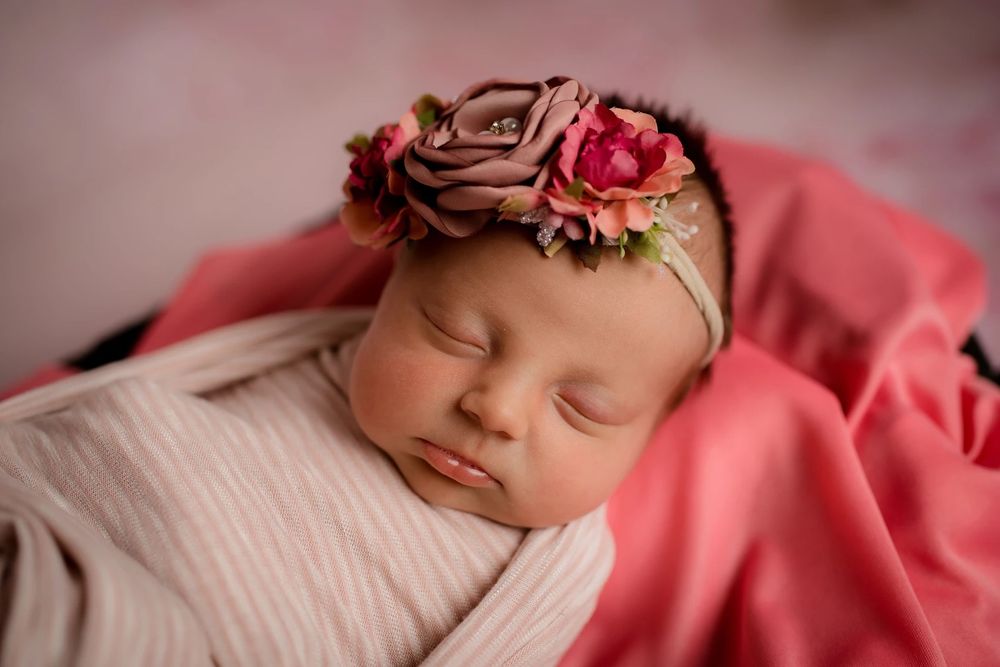 Peaceful newborn portrait with pink tones and floral accessories.
